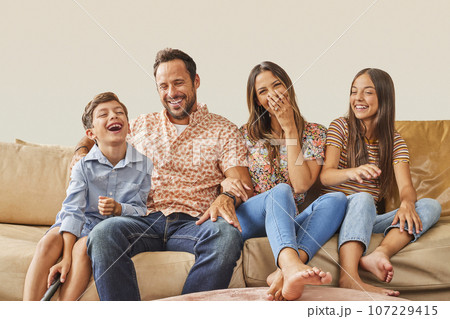 Smiling family with two children (8-9, 12-13) sitting on sofa Smiling family with two children (8-9, 12-13) sitting on sofa 107229415