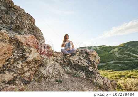 Mid adult woman meditating in mountains Mid adult woman meditating in mountains 107229484
