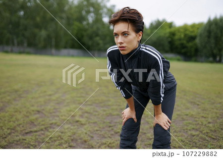 Portrait of young woman standing with hands on knees during sports training 107229882