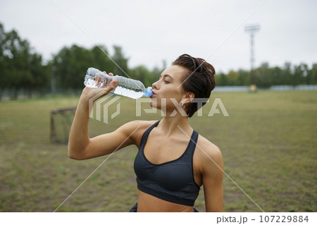 Young woman drinking water after sports training Young woman drinking water after sports training 107229884