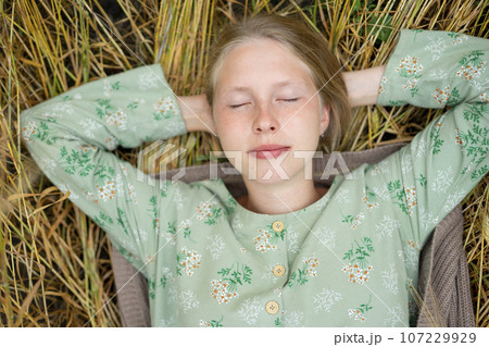 Young woman lying down in field with eyes closed  107229929