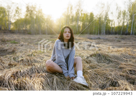 Brunette woman wearing grey sweatshirt sitting in meadow  107229943