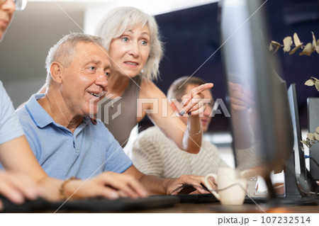 Older female mentor explaining something to elderly man at computer class 107232514