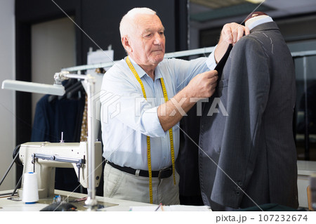 Experienced tailor tries on a new jacket on a mannequin in workshop 107232674