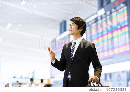 スマホを見ながら空港から出張をする若いビジネスマン スマホを見ながら空港から出張をする若いビジネスマン 107236321