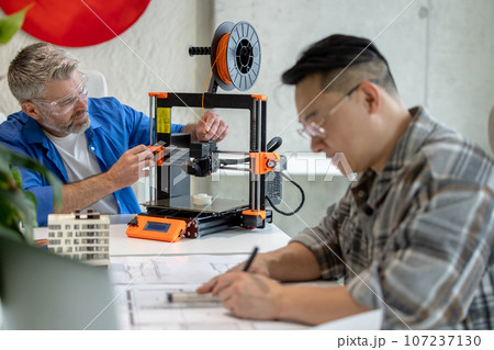 Architects working with 3D printer and projecting house model, drawing blueprint. Architects working with 3D printer and projecting house model, drawing blueprint. 107237130