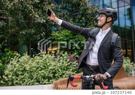 Smiling businessman in hemlet on a scooter making selfie Smiling businessman in hemlet on a scooter making selfie 107237140