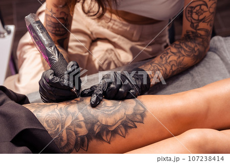 Professional tattoo master creating artistic masterpiece on female thigh 107238414