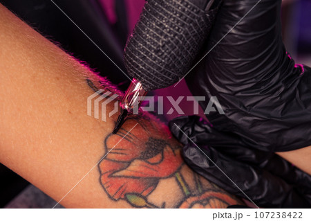 Tattoo machine in hands of professional master creating multicolored poppies 107238422