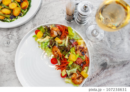 Salad with fried shrimp, mango, avocado and cherry tomatoes on a white plate 107238631