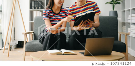 Two asian students learning together online with a laptop, tablet and tutor together in living room . 107241124