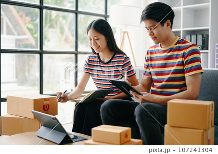 Starting small businesses SME owners, two check online orders Selling products working with boxs freelance work  on sofa at home using tablet and laptop  marketing, packaging, concept. 107241304