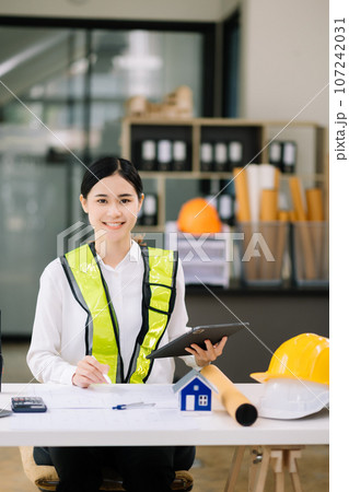 Creative architect projecting on the big drawings working and laptop with on on architectural project at construction at desk in office. Asian woman industry professional Creative architect projecting on the big drawings working and laptop with on on architectural project at construction at desk in office. Asian woman industry professional 107242031