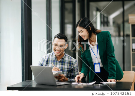 Asian business colleague business presents and explains and using laptop and tablet. Teamwork, financial marketing team, while sitting in modern office 107242163