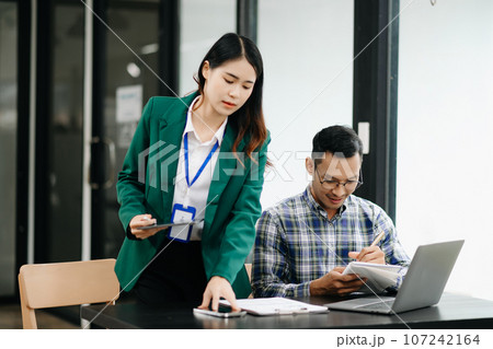 Asian business colleague business presents and explains and using laptop and tablet. Teamwork, financial marketing team, while sitting in modern office Asian business colleague business presents and explains and using laptop and tablet. Teamwork, financial marketing team, while sitting in modern office 107242164
