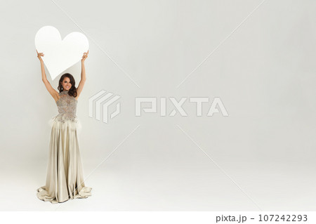 Perfect happy fashion model woman in luxurious dress holding empty white banner board Perfect happy fashion model woman in luxurious dress holding empty white banner board 107242293