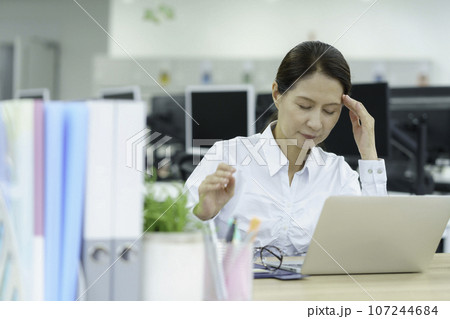 オフィスでこめかみを抑えるミドルエイジの女性 オフィスでこめかみを抑えるミドルエイジの女性 107244684