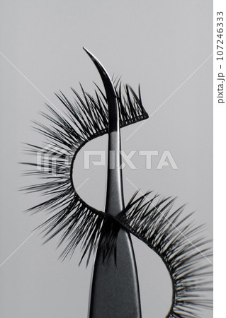 Makeup artist tools and accessories. Close-up image of metal tweezers with eyelashes for extension on gray background. 107246333