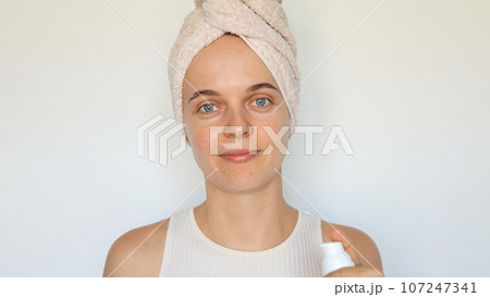 Cosmetic skincare routine. Health and beauty procedures. Smooth and clear skin. Wellness for face. Charming woman wrapped in bath towel holding bottle lotion isolated over white background 107247341