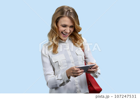 Young blonde woman playing video game on her smartphone. Isolated on blue. Young blonde woman playing video game on her smartphone. Isolated on blue. 107247531