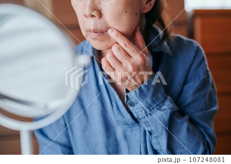 ほうれい線のしわを鏡で確認するシニア女性 107248081