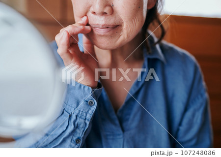 ほうれい線のしわを鏡で確認するシニア女性 107248086