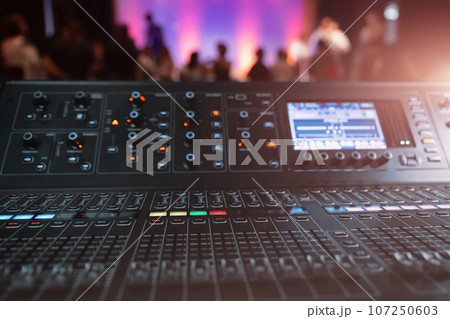 Live theater concert show sound video music control console with scene lights background. Sound engineer mixer soundboard equipment with many knobs, buttons, faders, equalizer screen and light Live theater concert show sound video music control console with scene lights background. Sound engineer mixer soundboard equipment with many knobs, buttons, faders, equalizer screen and light 107250603
