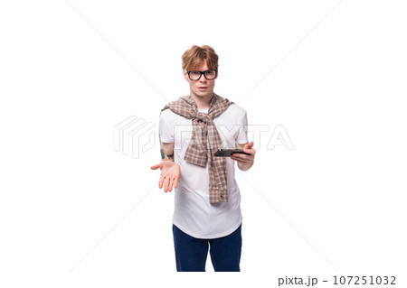 a handsome red-haired guy in glasses in a summer look is chatting on the phone 107251032
