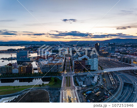 Aerial view of modern urban borough at Central train station against colourful sunset sky. Calm water surface reflecting sky. Oslo, Norway 107251946