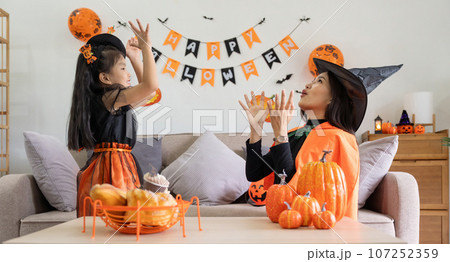 Happy family mother and child happy girl with Halloween at home together beautifully decorated. pretending to release air from a balloon at a child girl Happy family mother and child happy girl with Halloween at home together beautifully decorated. pretending to release air from a balloon at a child girl 107252359