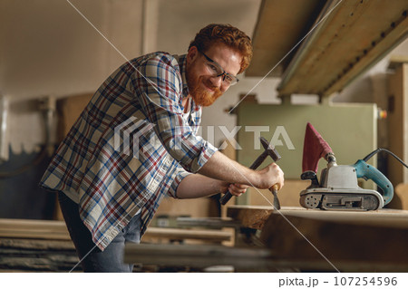 Professional craftsman working with chisel while cutting wooden plank in carpentry workshop Professional craftsman working with chisel while cutting wooden plank in carpentry workshop 107254596