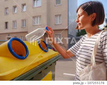 woman throwing plastic bottle Recycling bin stand on european street. Waste separation rubbish before drop to garbage bin to save world, environment care. Pollution trash recycling management concept 107255178