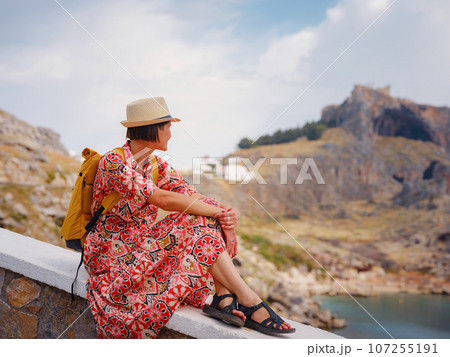 Nice Happy Female Enjoying Greek Islands. Travel to Greece, Mediterranean islands outside tourist season. Having fun at stunning view on sea resort and old town of Lindos on mountain Nice Happy Female Enjoying Greek Islands. Travel to Greece, Mediterranean islands outside tourist season. Having fun at stunning view on sea resort and old town of Lindos on mountain 107255191