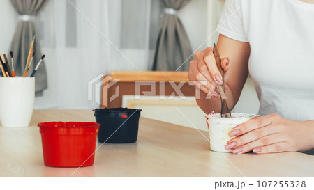 Paint drawing. Artistic equipment. Unrecognizable woman painter hands mixing colors dipping in can brush at table in studio. 107255328