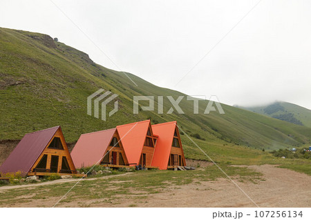 a-frame triangular houses in mountains, around rocks and green grass 107256134