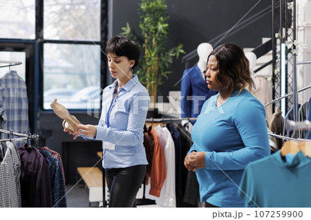 African american customer asking store employee for help with elegant shoes, discussing fabric before buying it. Stylish woman shopping for fashionable clothes in modern boutique. Fashion concept 107259900