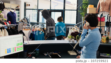 African american robber stealing basic shirt in modern boutique, being caught by asian security guard. Thief running from bodyguard, trying to escape the accusations. Crime concept 107259921