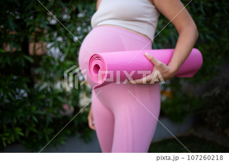 a young pregnant woman holds a pink yoga mat in her hands. close-up shot a young pregnant woman holds a pink yoga mat in her hands. close-up shot 107260218