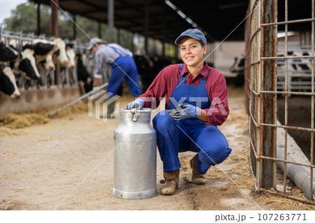 Female owner with milk can standing in stall on background with herd of cows 107263771