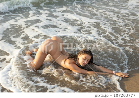 Young nude woman posing kneeling on beach 107263777