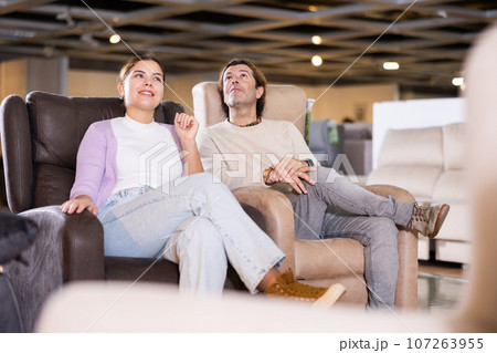 Guy and girl sitting in armchairs and deciding on buying in furniture section Guy and girl sitting in armchairs and deciding on buying in furniture section 107263955