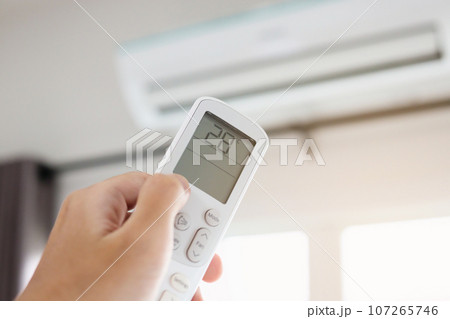 Hand with remote control directed on air conditioner inside the room 107265746