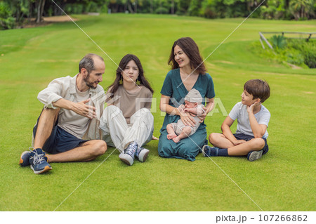 Happy couple in their 40s, surrounded by adult children, cradle a newborn in a sunlit park. Love, family, and generations in harmony Happy couple in their 40s, surrounded by adult children, cradle a newborn in a sunlit park. Love, family, and generations in harmony 107266862