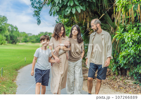 Happy couple in their 40s, surrounded by adult children, cradle a newborn in a sunlit park. Love, family, and generations in harmony 107266889