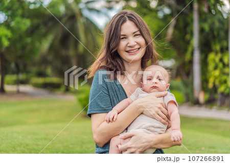 A happy 40-year-old mother cradles her newborn in a sun-drenched park. Love, family and generations in harmony 107266891