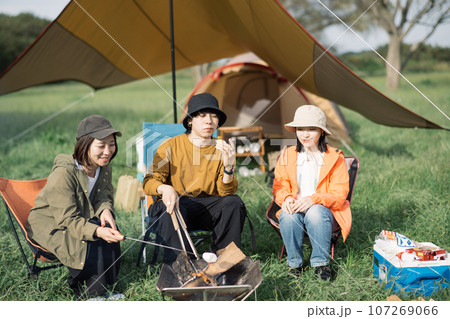 キャンプを楽しむ若い男女・焚き火・焼きマシュマロをするアウトドアイメージ 107269066