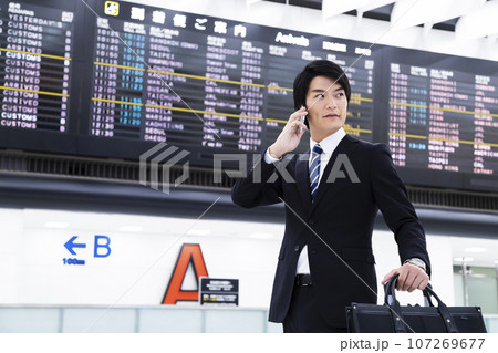 スマホを見ながら空港から出張をする若いビジネスマン 107269677