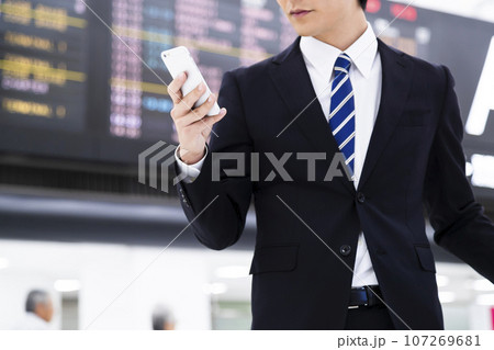 スマホを見ながら空港から出張をする若いビジネスマン スマホを見ながら空港から出張をする若いビジネスマン 107269681