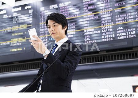 スマホを見ながら空港から出張をする若いビジネスマン スマホを見ながら空港から出張をする若いビジネスマン 107269697