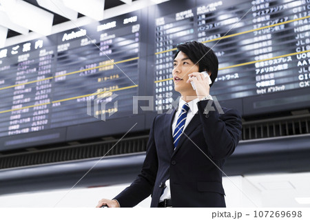 スマホを見ながら空港から出張をする若いビジネスマン 107269698